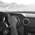Black and white stock image of person driving left hand drive car - can see steering wheel and dashboard.